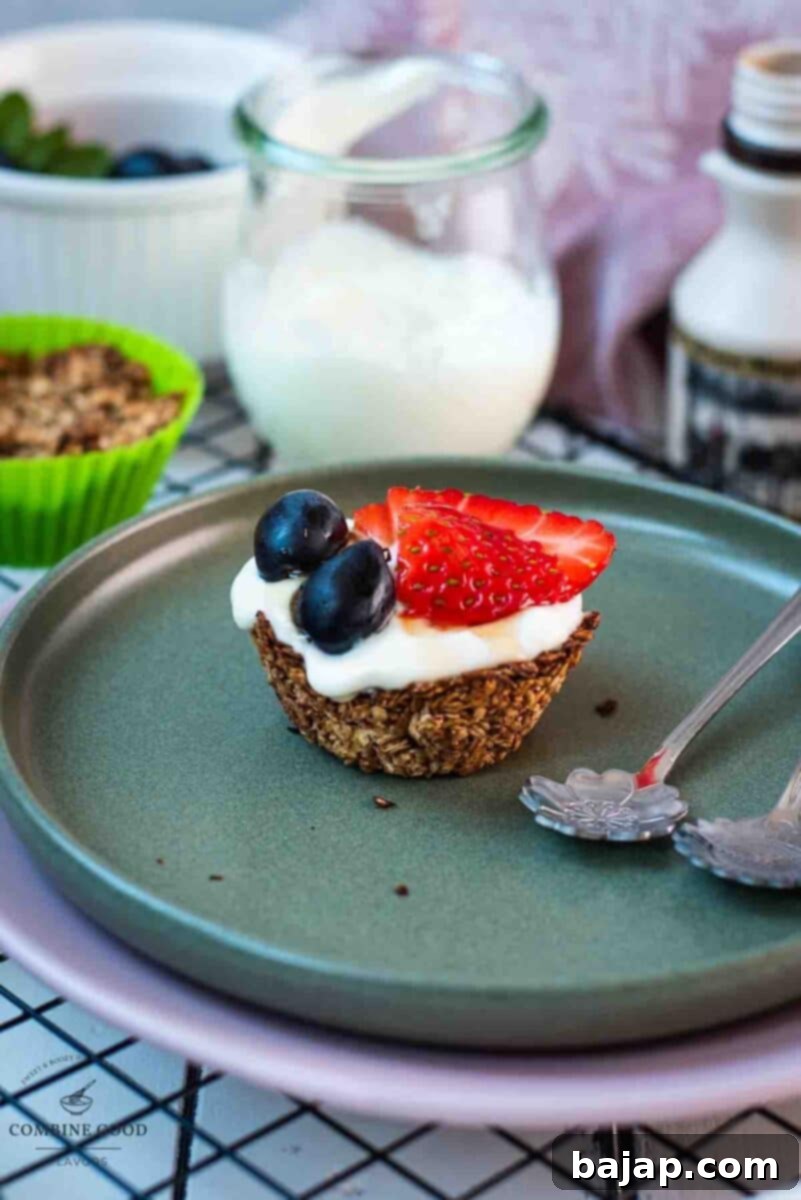 Crunchy Granola Bites 2 Cute little granola cup, filled with creamy yogurt and topped with fresh, vibrant strawberries, juicy blue grapes, and drizzled with glistening maple syrup. Placed elegantly on a dark green plate, ready to be enjoyed as a perfect morning treat.