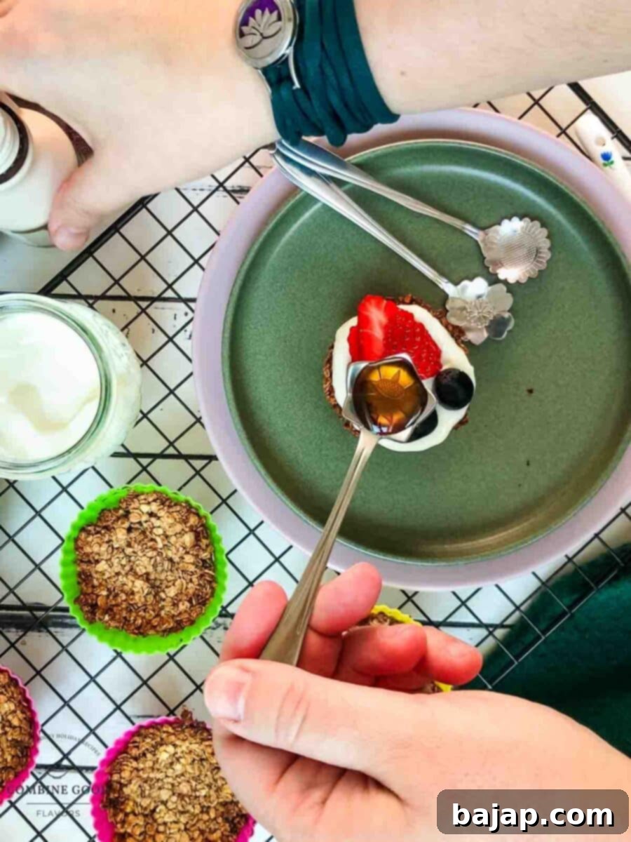 Crunchy Granola Bites 11 A final drizzle of rich maple syrup is being poured over the granola cups, topped with yogurt and fresh fruit, adding a beautiful glaze and extra sweetness.
