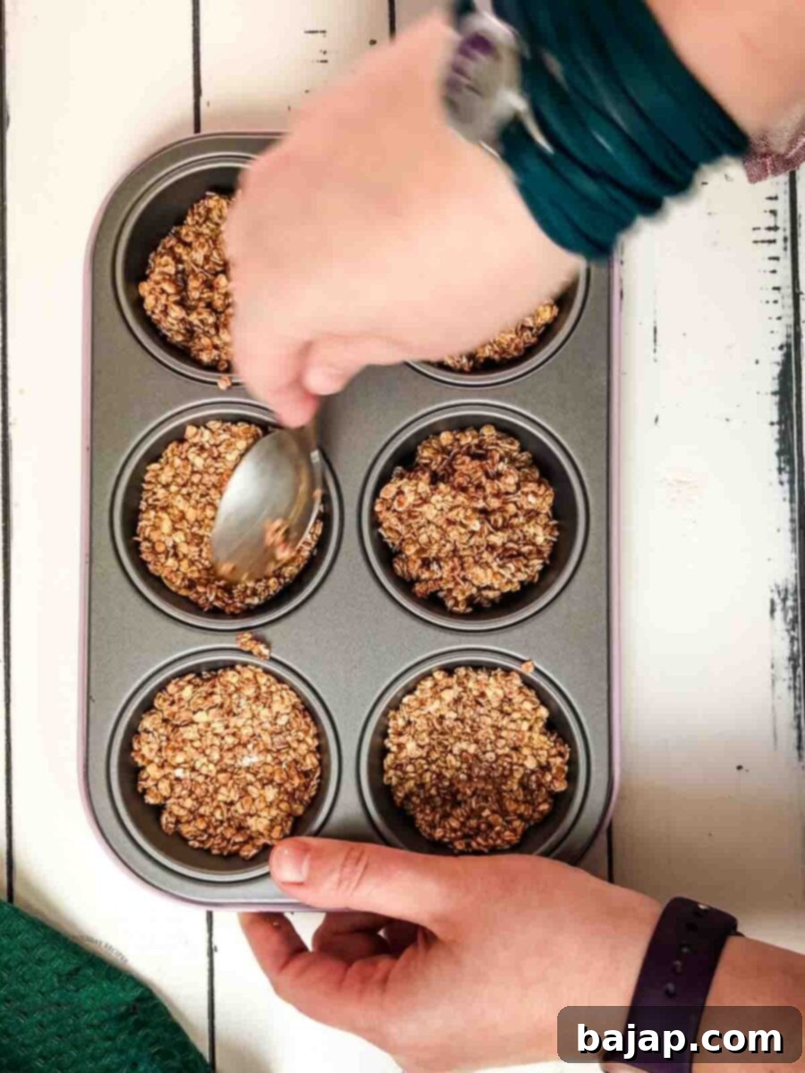 Crunchy Granola Bites 6 A hand is gently but firmly pressing the granola mixture into the silicone muffin tin molds, shaping it into perfect little cups.
