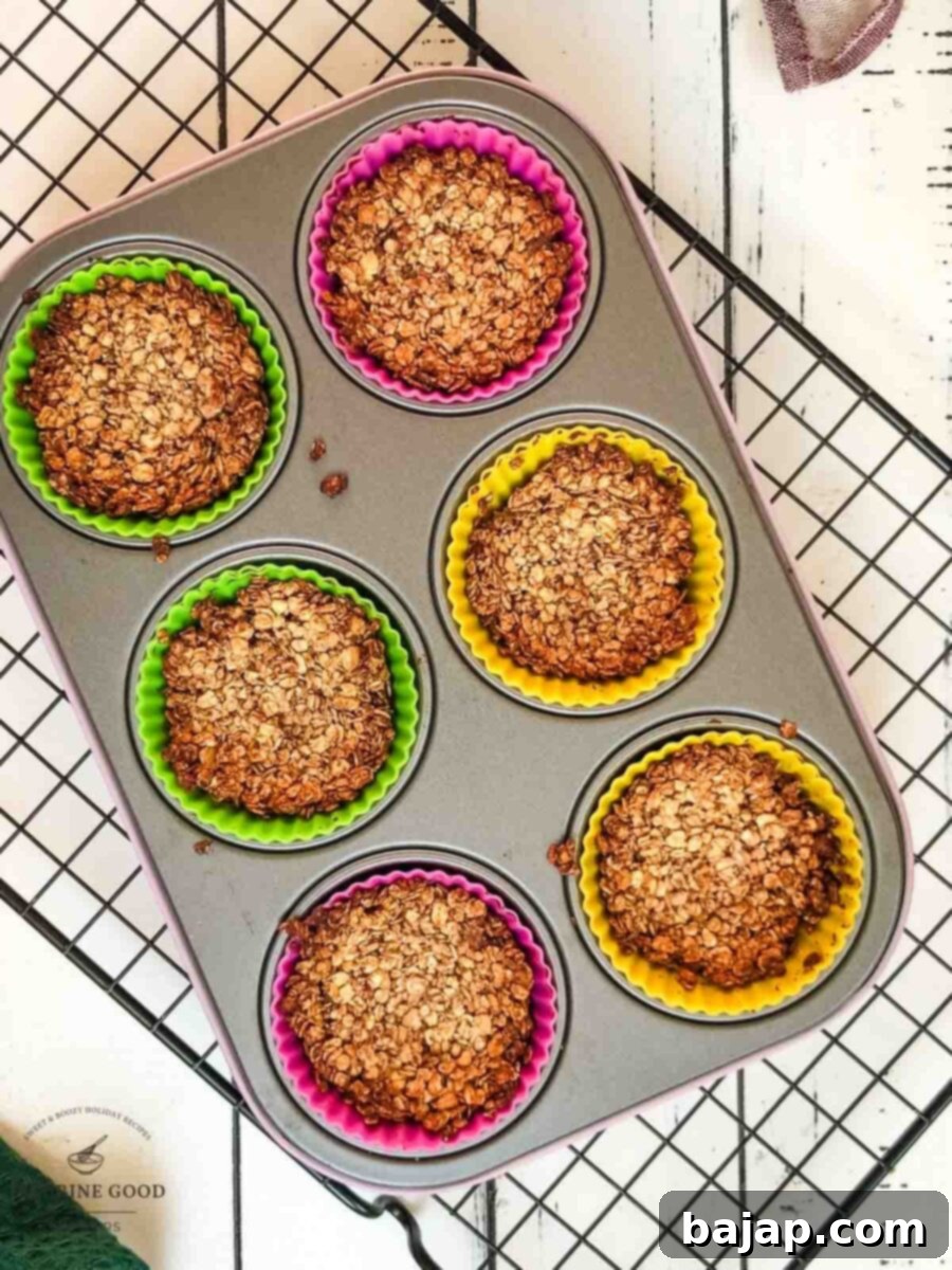 Crunchy Granola Bites 7 A muffin tin filled with baked granola cups in silicone molds, cooling on a wire rack after being removed from the oven.