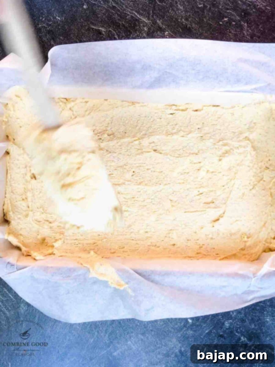 Spreading Funfetti cookie dough evenly into a parchment-lined 9x13 inch baking pan for uniform baking.