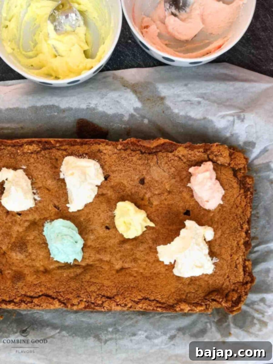 Dolloping pastel colored buttercream strategically across cooled Funfetti cookie bars.