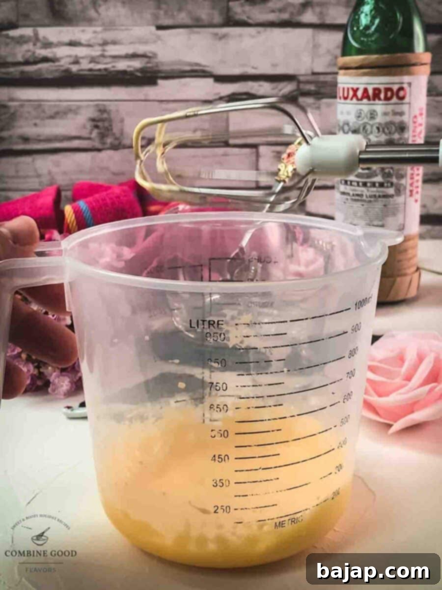 Egg yolk powdered sugar mixture in a mixing bowl next to a hand mixer.