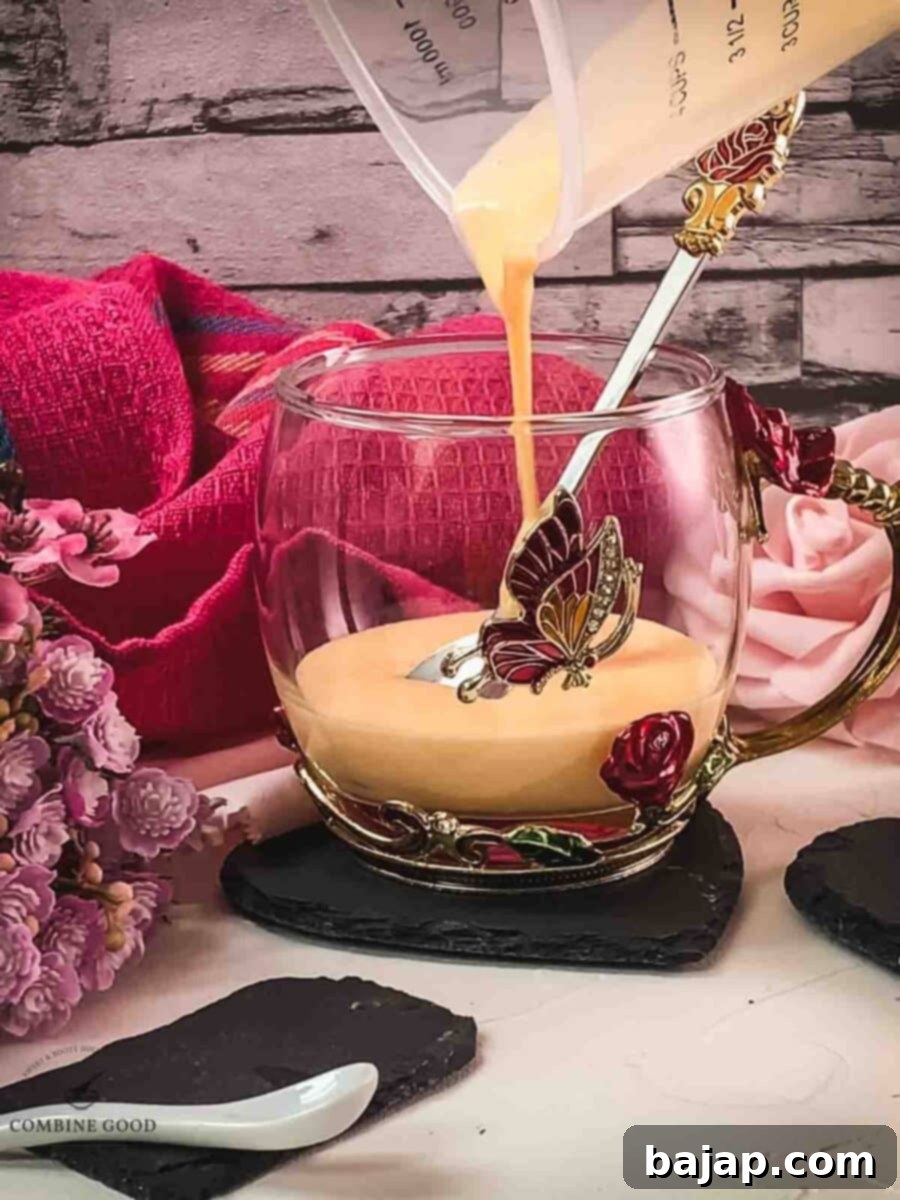 Pouring the whipped egg yolk, powdered sugar, and Maraschino mixture into a serving glass for the warm cocktail.