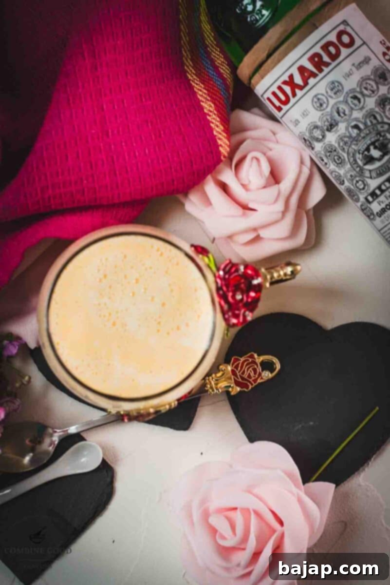 Creamy, dreamy Maraschino liqueur cocktail served in whimsical cup with red and golden butterflies and flowers. Placed on a black slate heart shaped coaster.