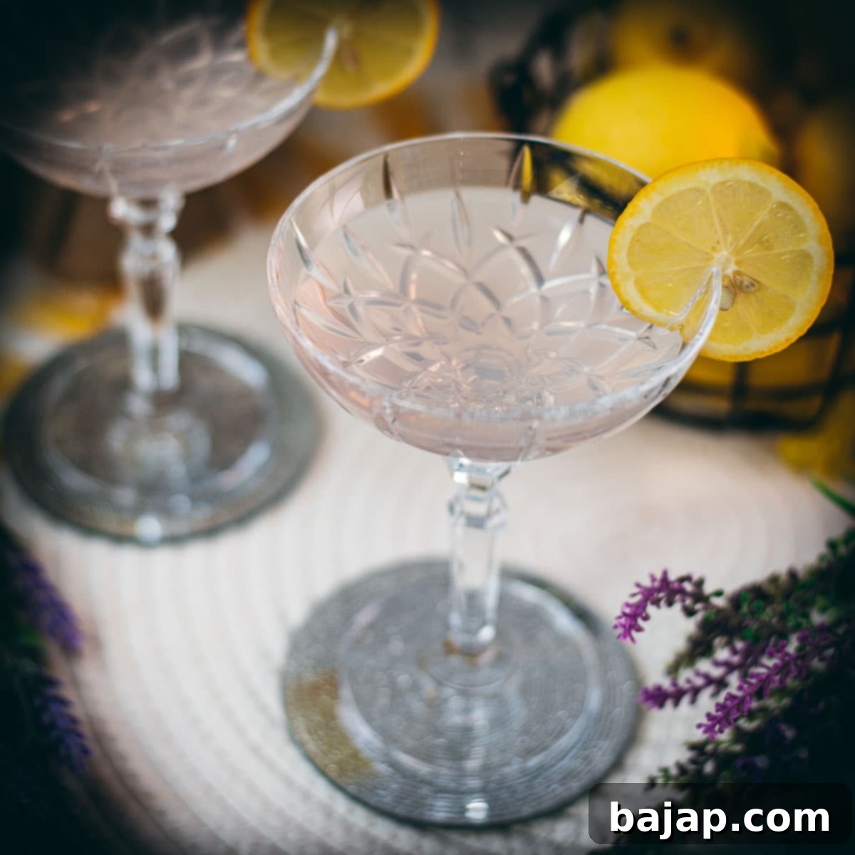 Elegant lavender gin spritz cocktail with prosecco, placed on a mirrored coaster, garnished with a lemon slice.