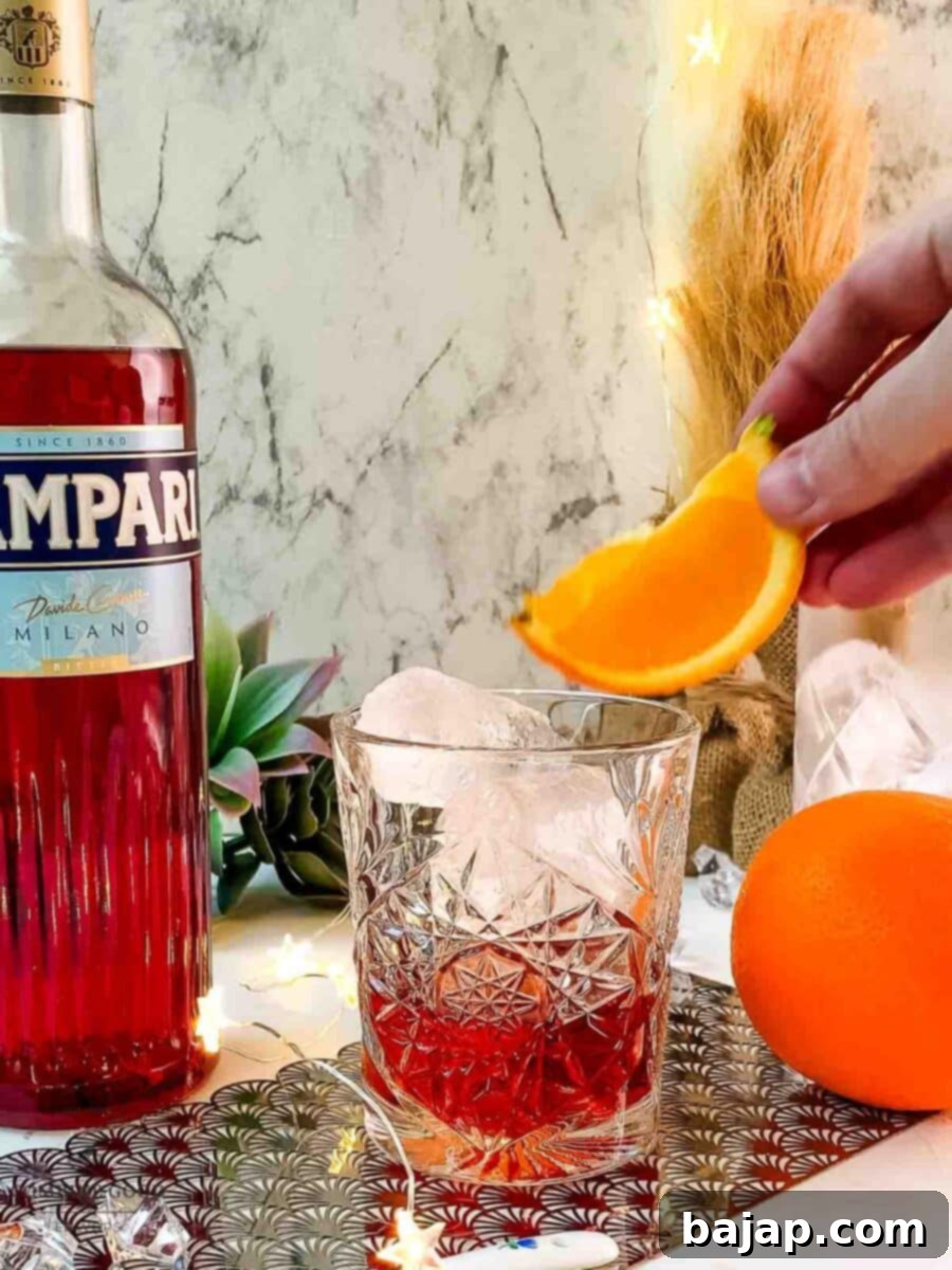 Hand placing orange wedge on top of the Negroni cocktail.