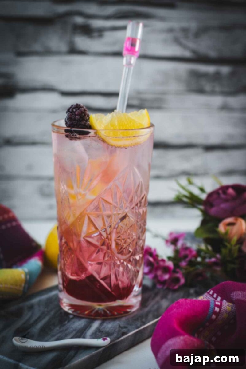 Refreshing blackberry raspberry gin fizz, garnished with a lemon wedge and a blackberry, placed on marbled plate.