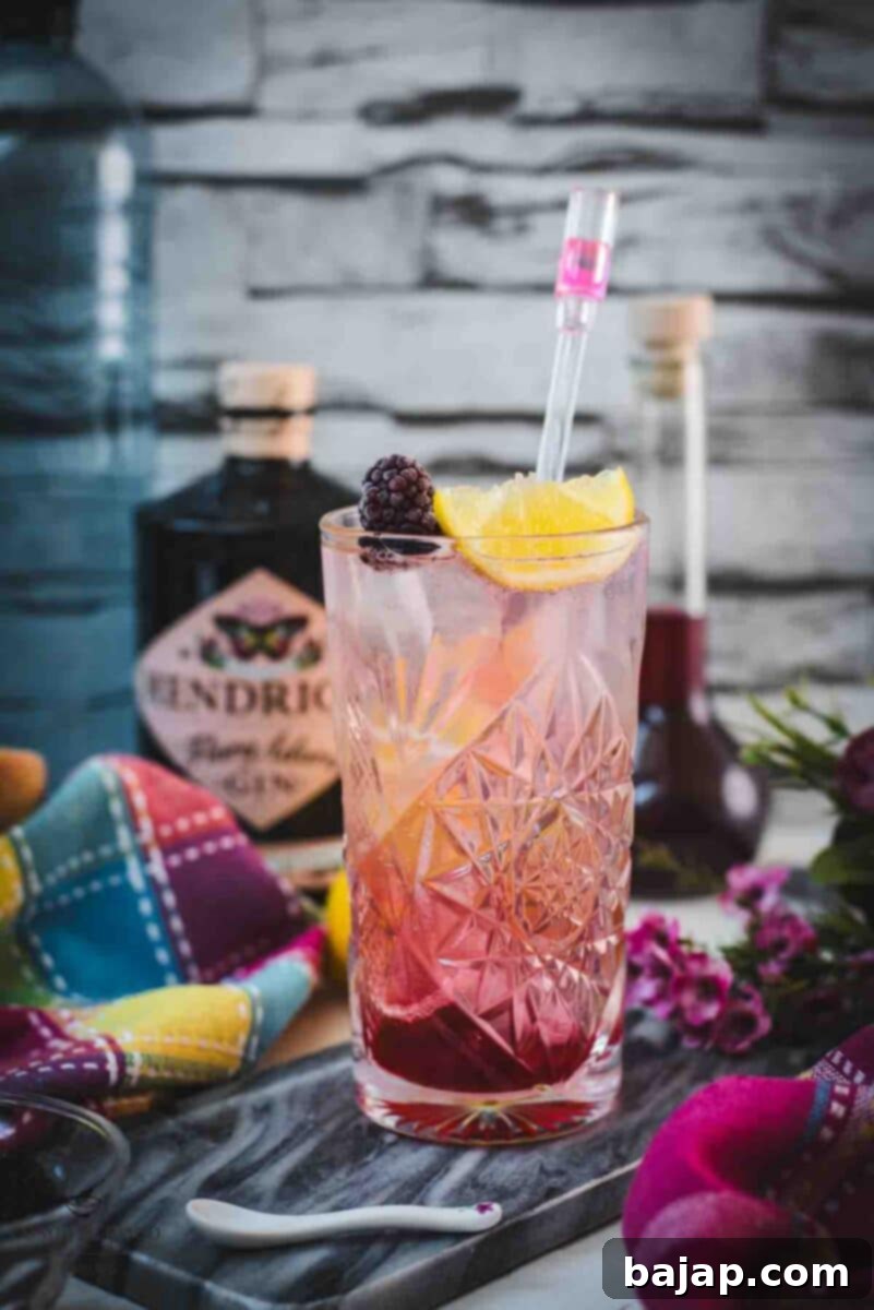A refreshing Blackberry Raspberry Gin Fizz, garnished with a lemon wedge and a fresh blackberry, sitting elegantly on a marbled plate, inviting you to enjoy its vibrant flavors.