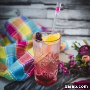 Refreshing blackberry raspberry gin fizz, garnished with a lemon wedge and a blackberry, placed on marbled plate.