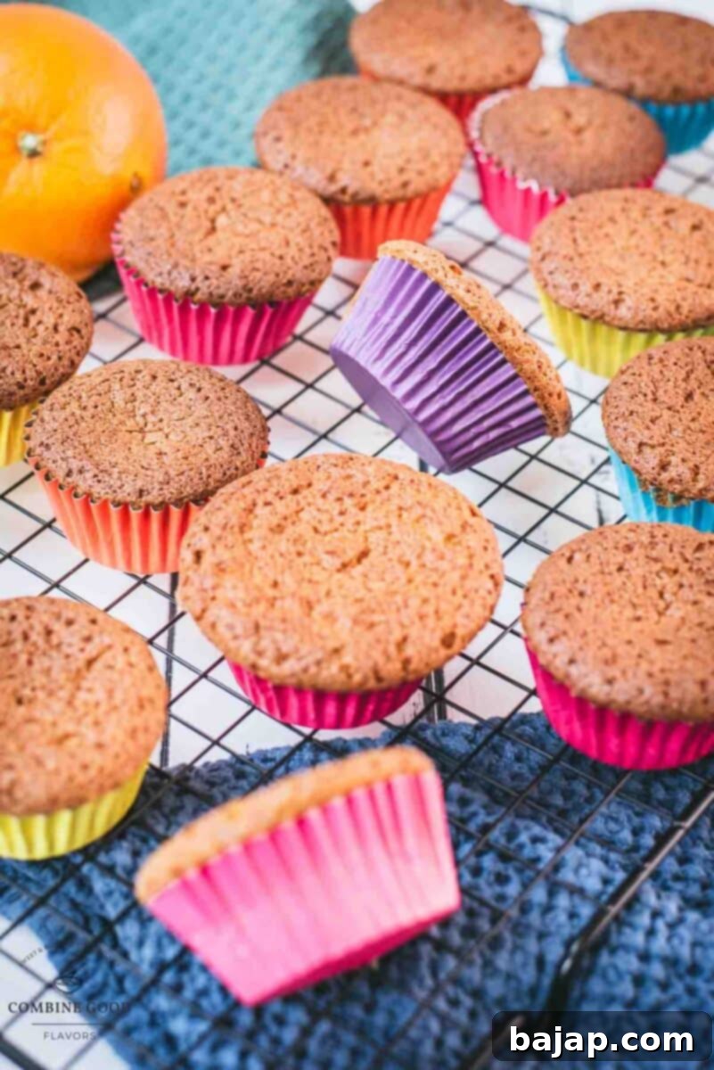 Close-up of fluffy orange muffins cooling on a metal wire rack, showcasing their golden color and perfect dome tops.