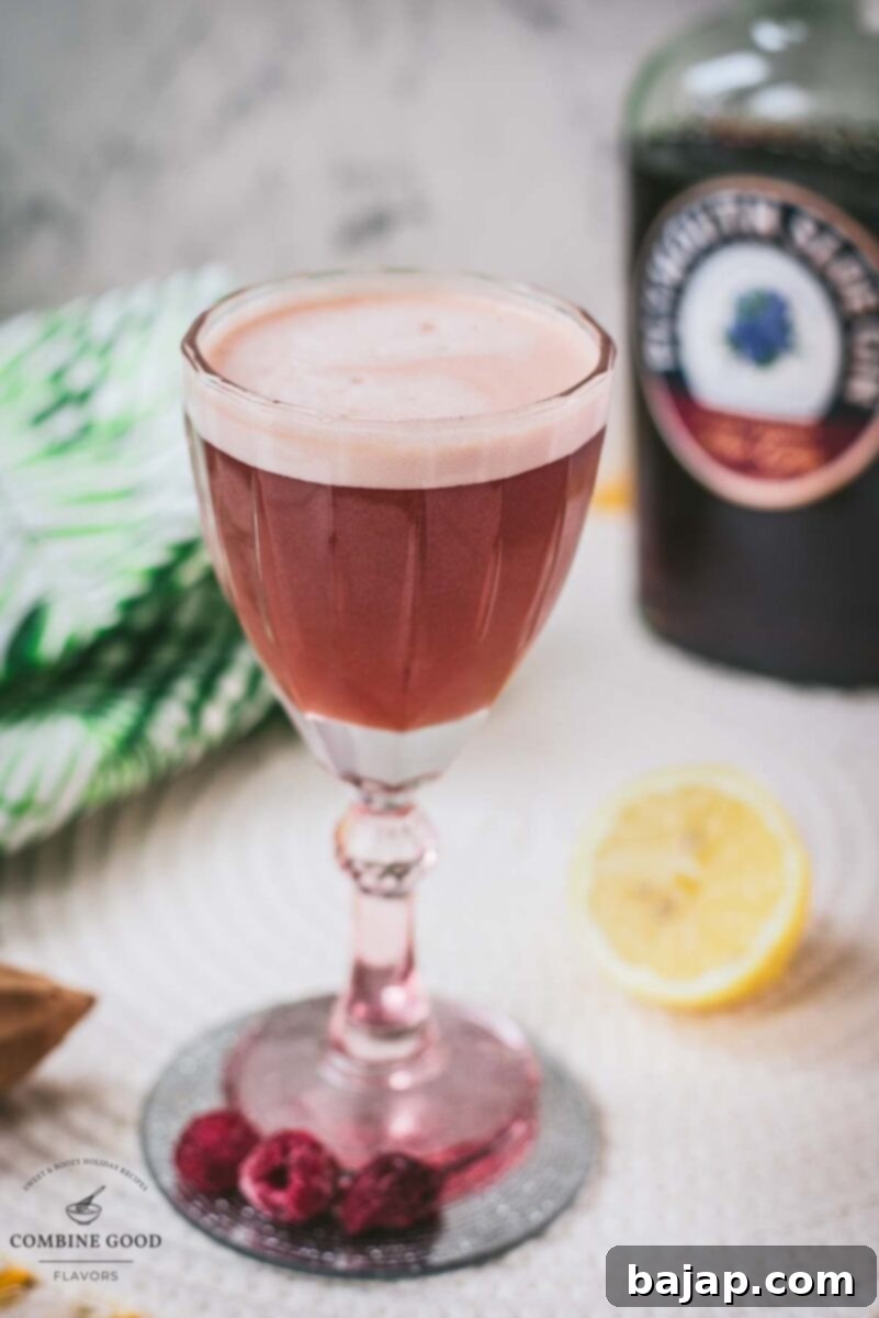 Divine ruby fizz cocktail, elegantly presented with its signature foam, placed on a mirrored coaster.