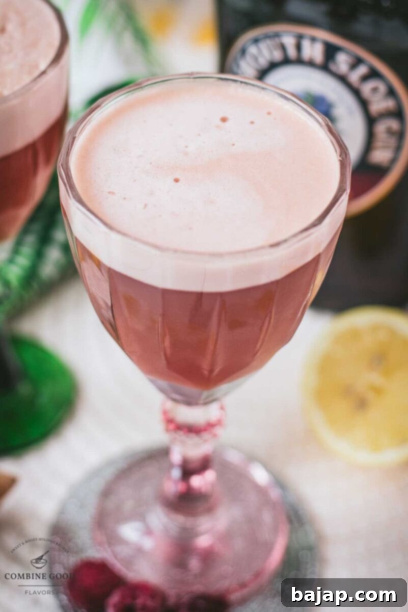 The stunning Ruby Fizz cocktail, presented on a mirrored coaster and served in beautifully mismatched red and green glasses, ready to be enjoyed.