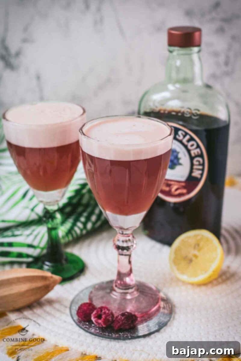 Divine ruby fizz cocktail, showcasing the beautiful foam, placed on a mirrored coaster and served in a red and a green glass.