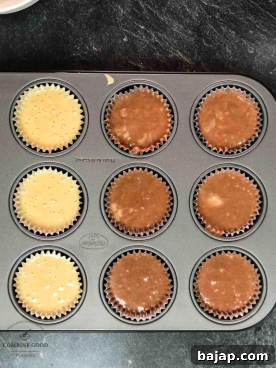 Muffin tin with paper liners, filled generously with alternating scoops of light vanilla rum batter and dark cocoa rum batter, ready for baking.