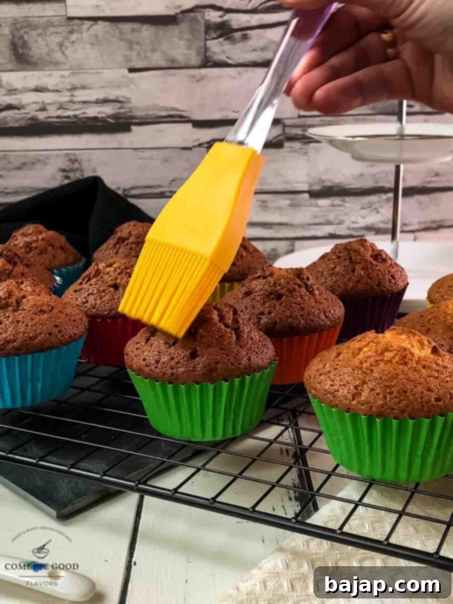 A hand brushing the top of a warm, freshly baked rum muffin with white rum, creating a glossy finish and enhancing the boozy aroma.