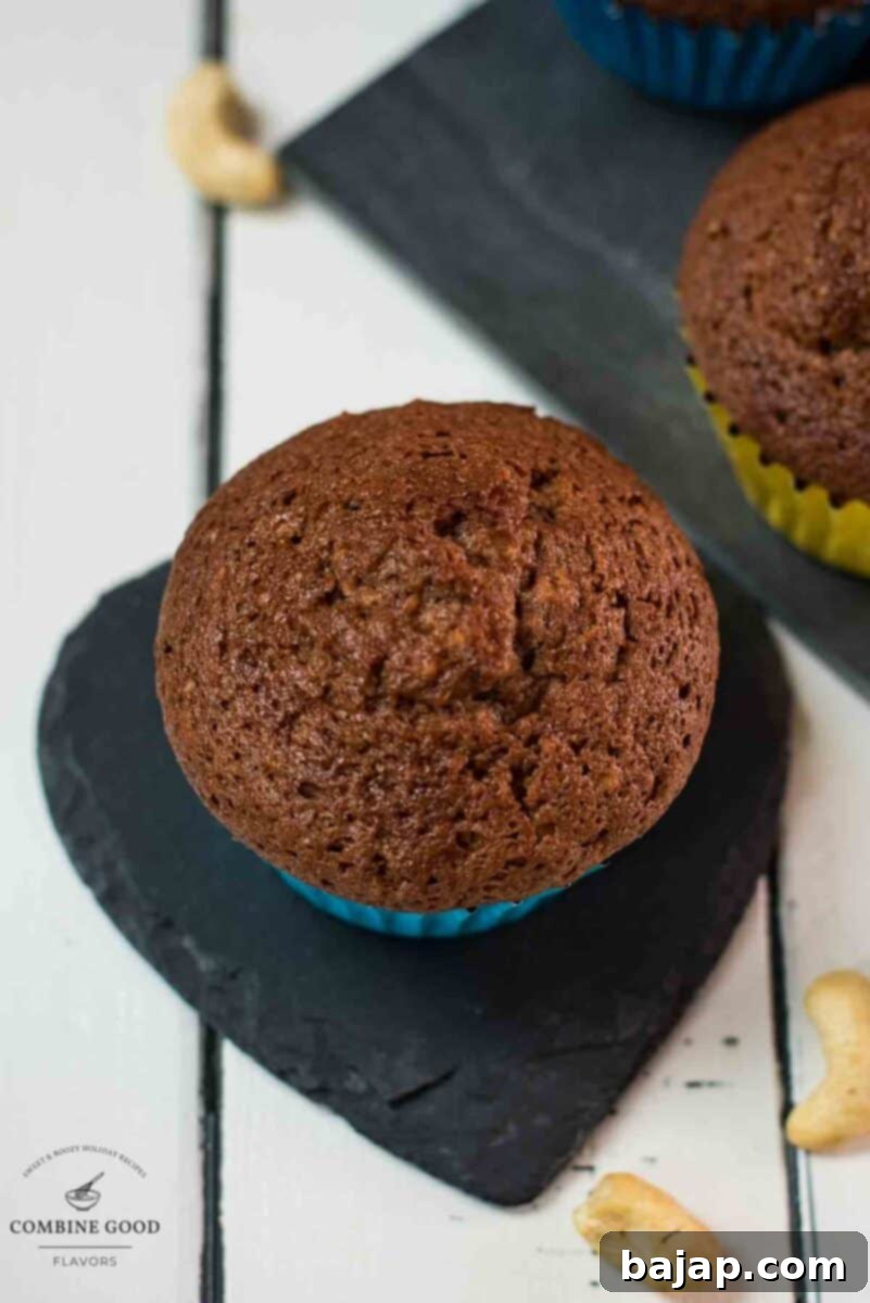 A single, perfectly baked rum muffin, garnished with a sprinkle of nuts, rests elegantly on a heart-shaped black slate coaster, highlighting its golden-brown exterior and inviting texture.