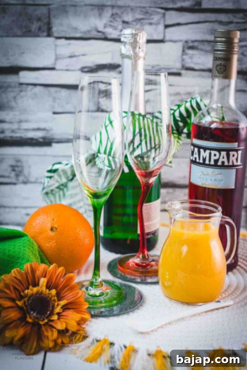 Essential Campari Mimosa ingredients: a bottle of vibrant red Campari, fresh oranges for juice, and a bottle of chilled Prosecco.
