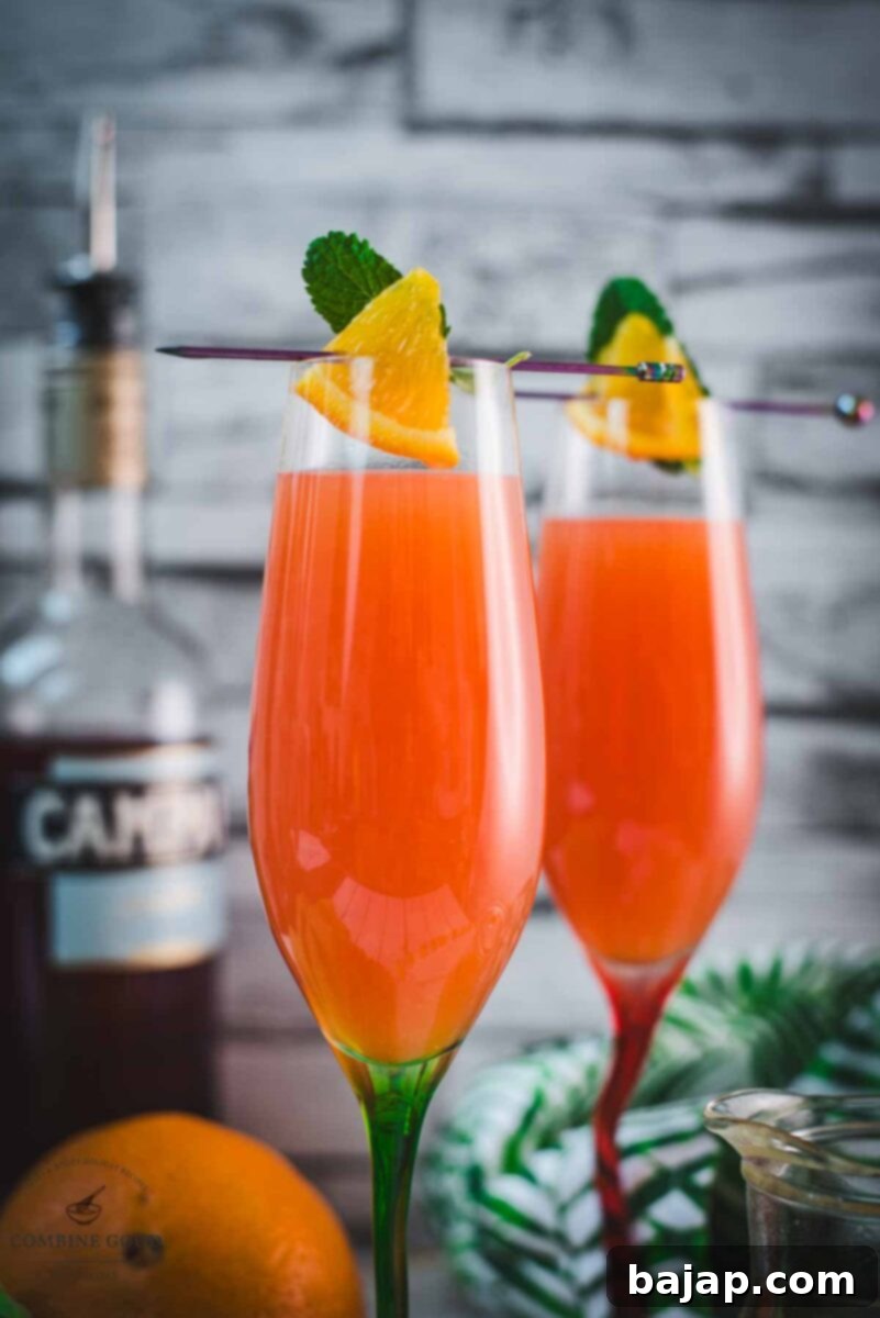 A perfectly prepared Campari Mimosa in a champagne flute with a vibrant orange and mint garnish, ready for a special occasion.