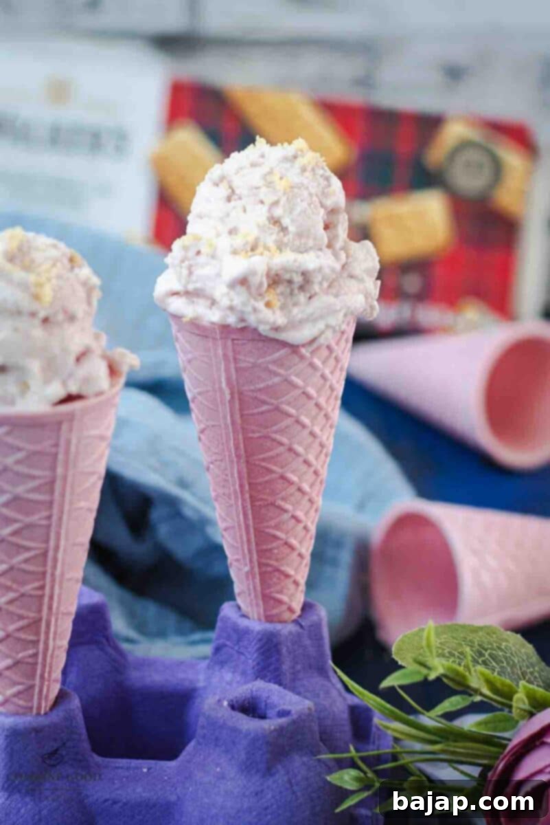 Two pink ice cream cones filled with strawberry shortcake ice cream, sprinkled with shortbread crumbs.