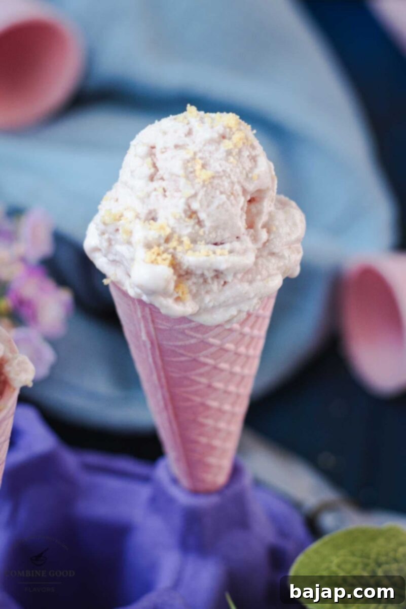 Pink ice cream cone filled with strawberry shortcake ice cream, sprinkled with shortbread crumbs.