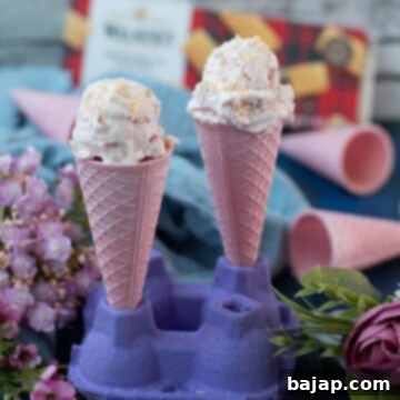 Two pink ice cream cones filled with strawberry shortcake ice cream, sprinkled with shortbread crumbs.