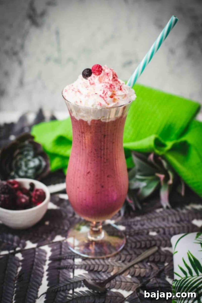 Boozy berry adult milkshake with homemade Chambord, served in Hurricane glass. Garnished with whipped cream, a black and a red currant and dusted with edible glitter. Served with a drinking straw.