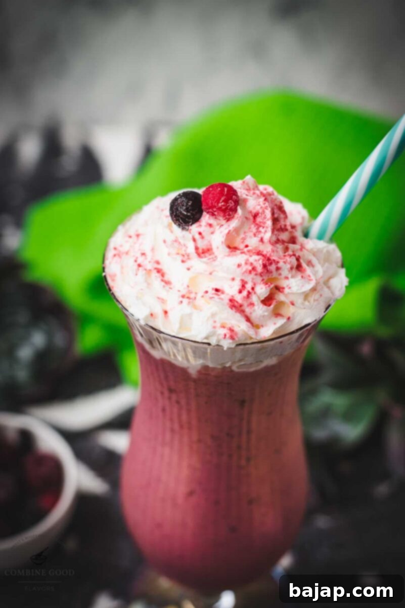 Boozy berry adult milkshake with homemade Chambord, served in Hurricane glass. Garnished with whipped cream, a black and a red currant and dusted with edible glitter. Served with a drinking straw.
