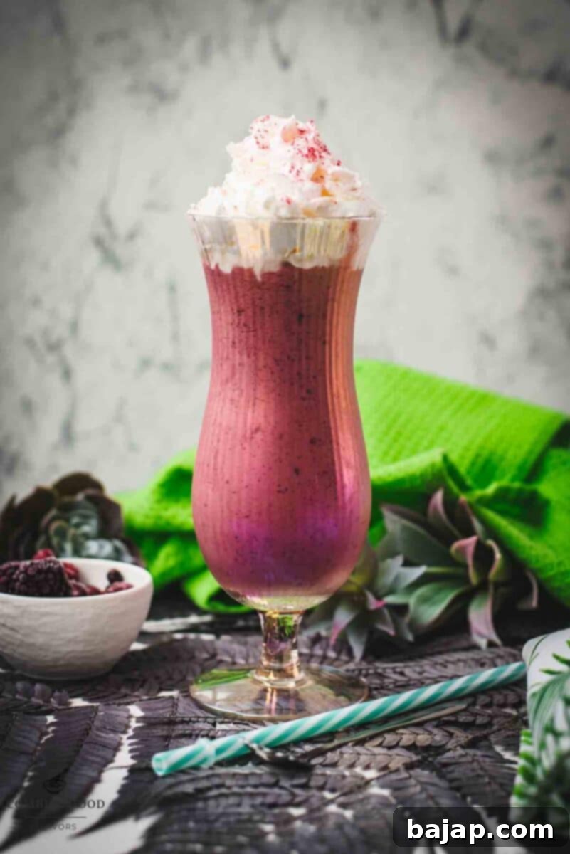Boozy berry adult milkshake with homemade Chambord, served in Hurricane glass. Garnished with whipped cream and dusted with edible glitter. Served with a drinking straw.