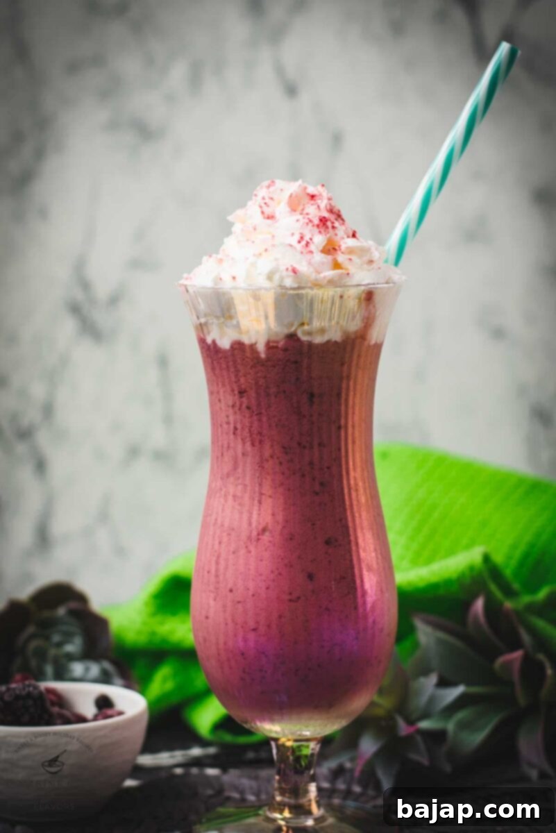 Boozy berry adult milkshake with homemade Chambord, served in Hurricane glass. Garnished with whipped cream and dusted with edible glitter. Served with a drinking straw.