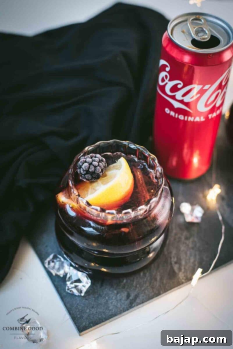 Cute glass filled with a delicious chambord coke cocktail, placed on black slate plate and garnished with a lemon wedge and one frozen blackberry.