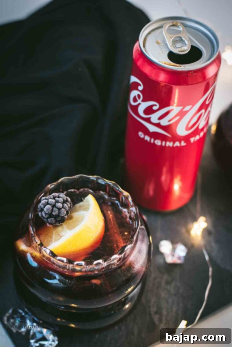 Cute glass filled with a delicious chambord coke cocktail, placed on black slate plate and garnished with a lemon wedge and one frozen blackberry.