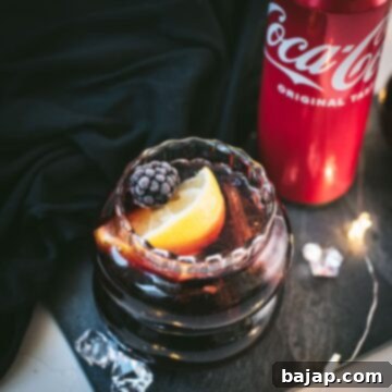 Cute glass filled with a delicious chambord coke cocktail, placed on black slate plate and garnished with a lemon wedge and one frozen blackberry.
