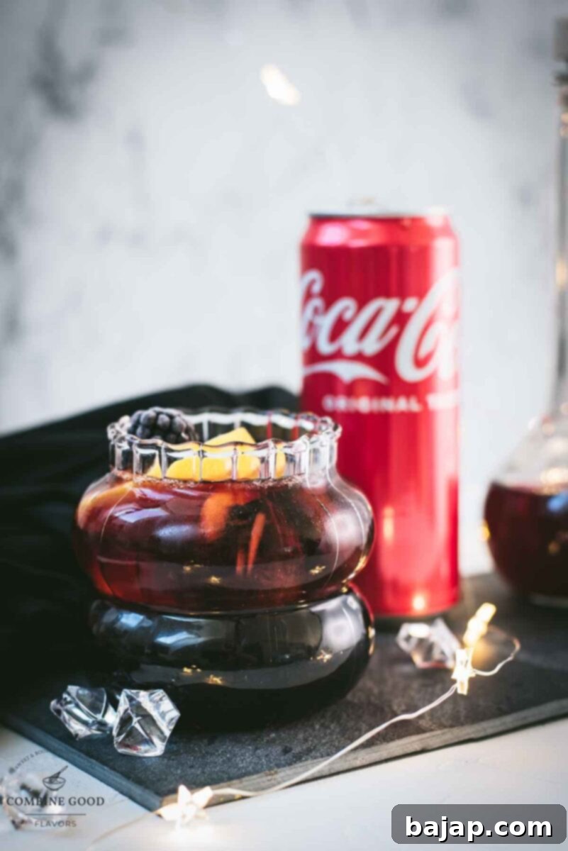 Cute glass filled with a delicious chambord coke cocktail, placed on black slate plate and garnished with a lemon wedge and one frozen blackberry.