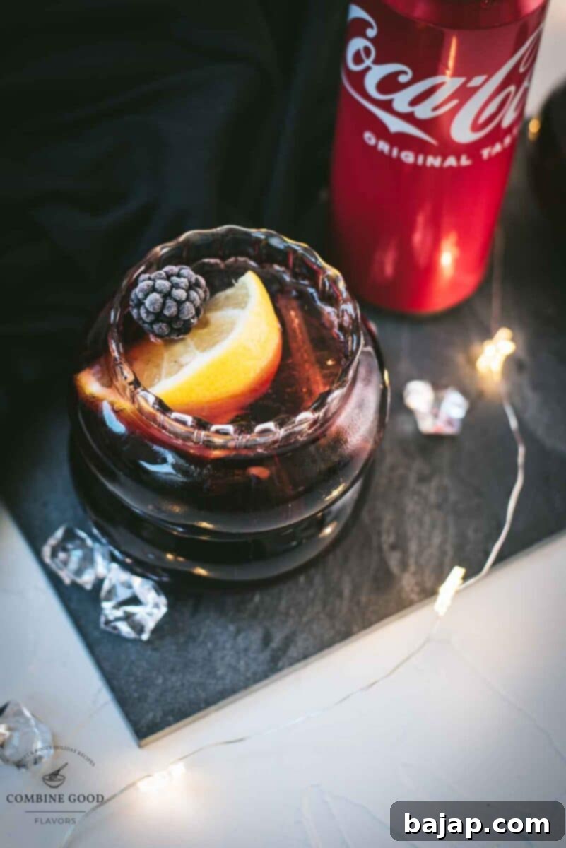 Cute glass filled with a delicious chambord coke cocktail, placed on black slate plate and garnished with a lemon wedge and one frozen blackberry.