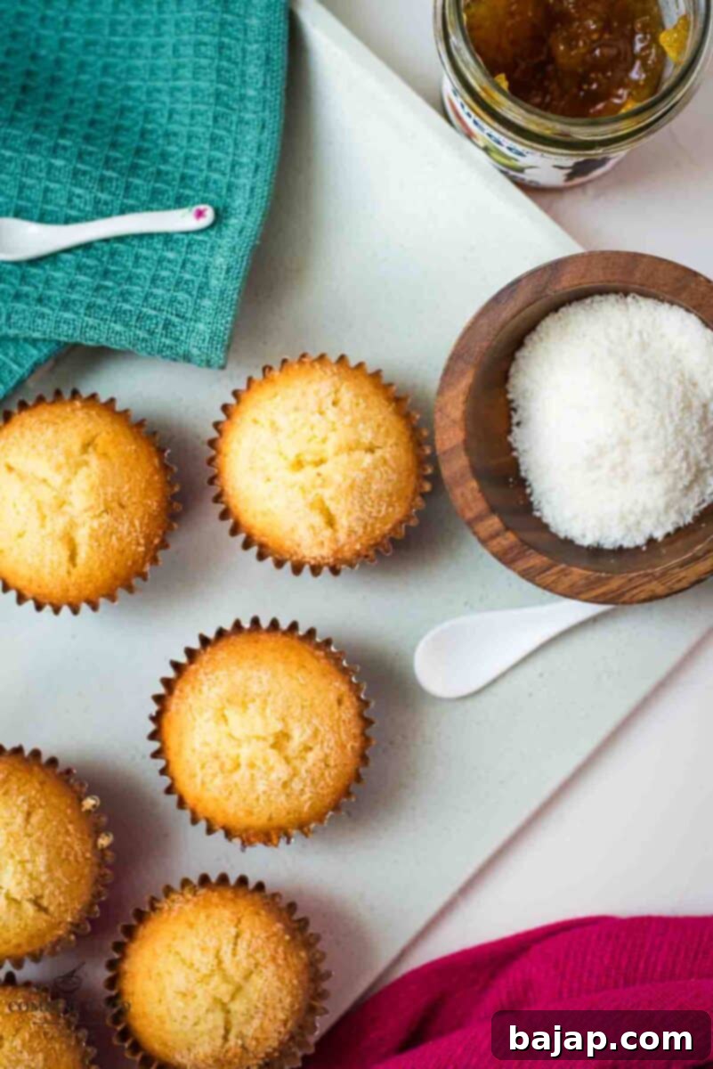 A stunning arrangement of golden-brown fig jam-filled coconut muffins on a white serving plate, garnished with fresh coconut flakes.