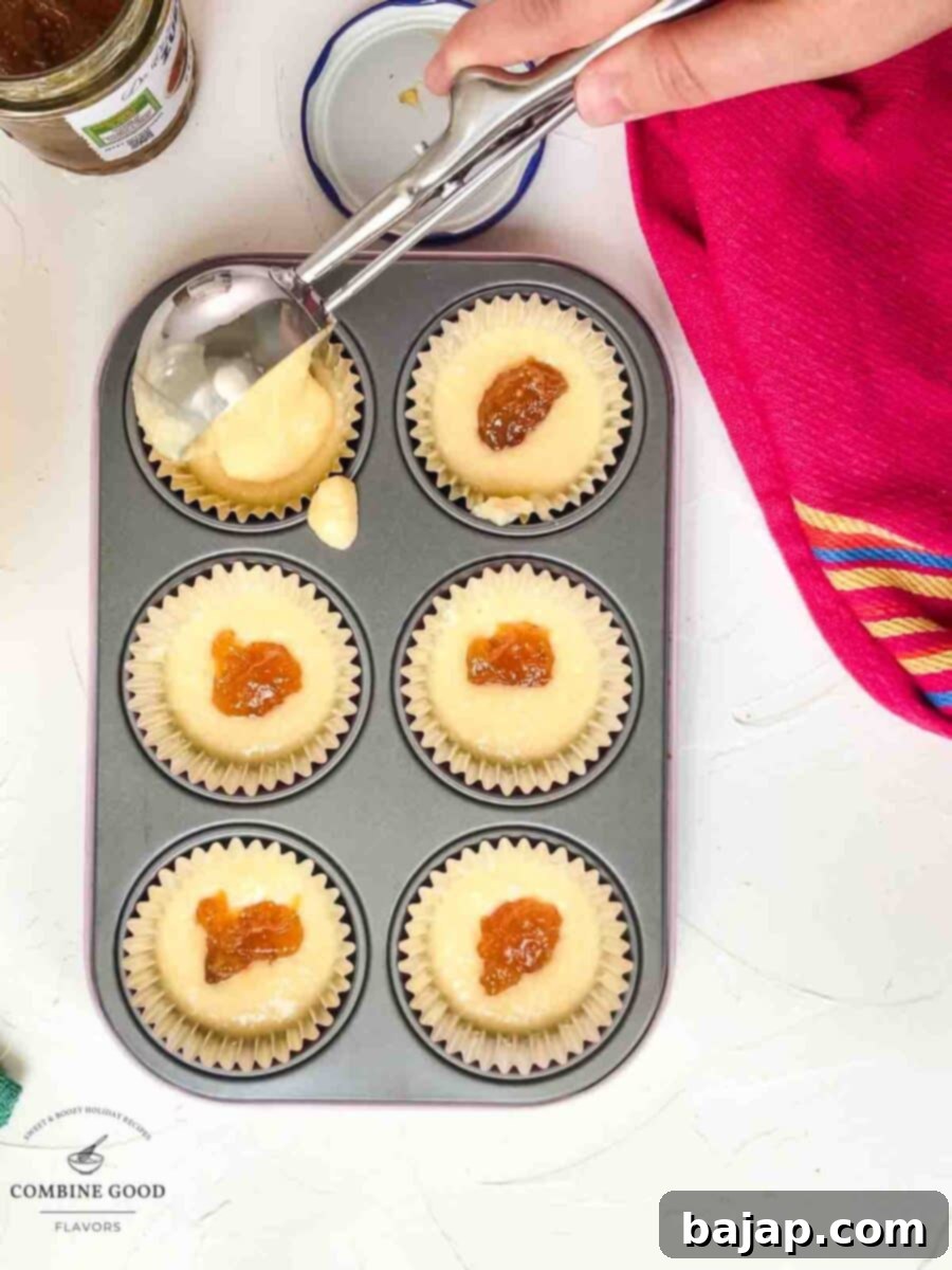Muffin cups now fully covered with batter, concealing the fig jam centers, ready for topping.