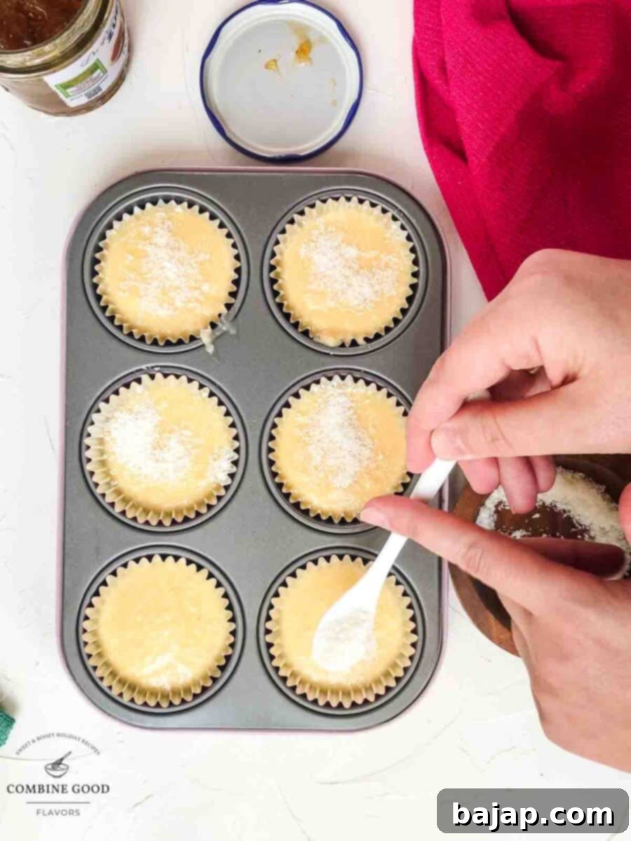 Unbaked coconut muffins topped with a sprinkle of shredded coconut, ready for the oven.