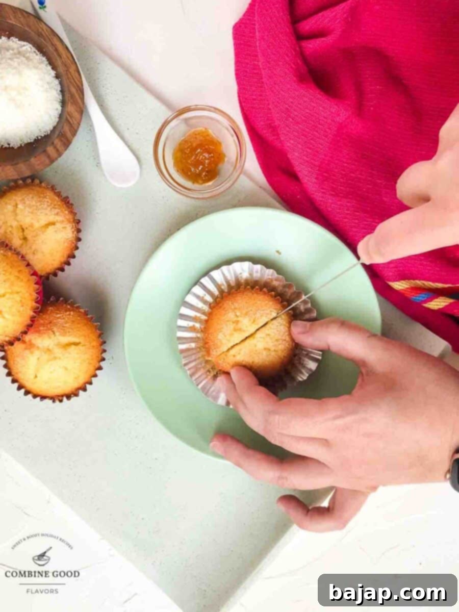 A knife gently dividing a warm coconut muffin in half, preparing to reveal the delicious fig jam inside.