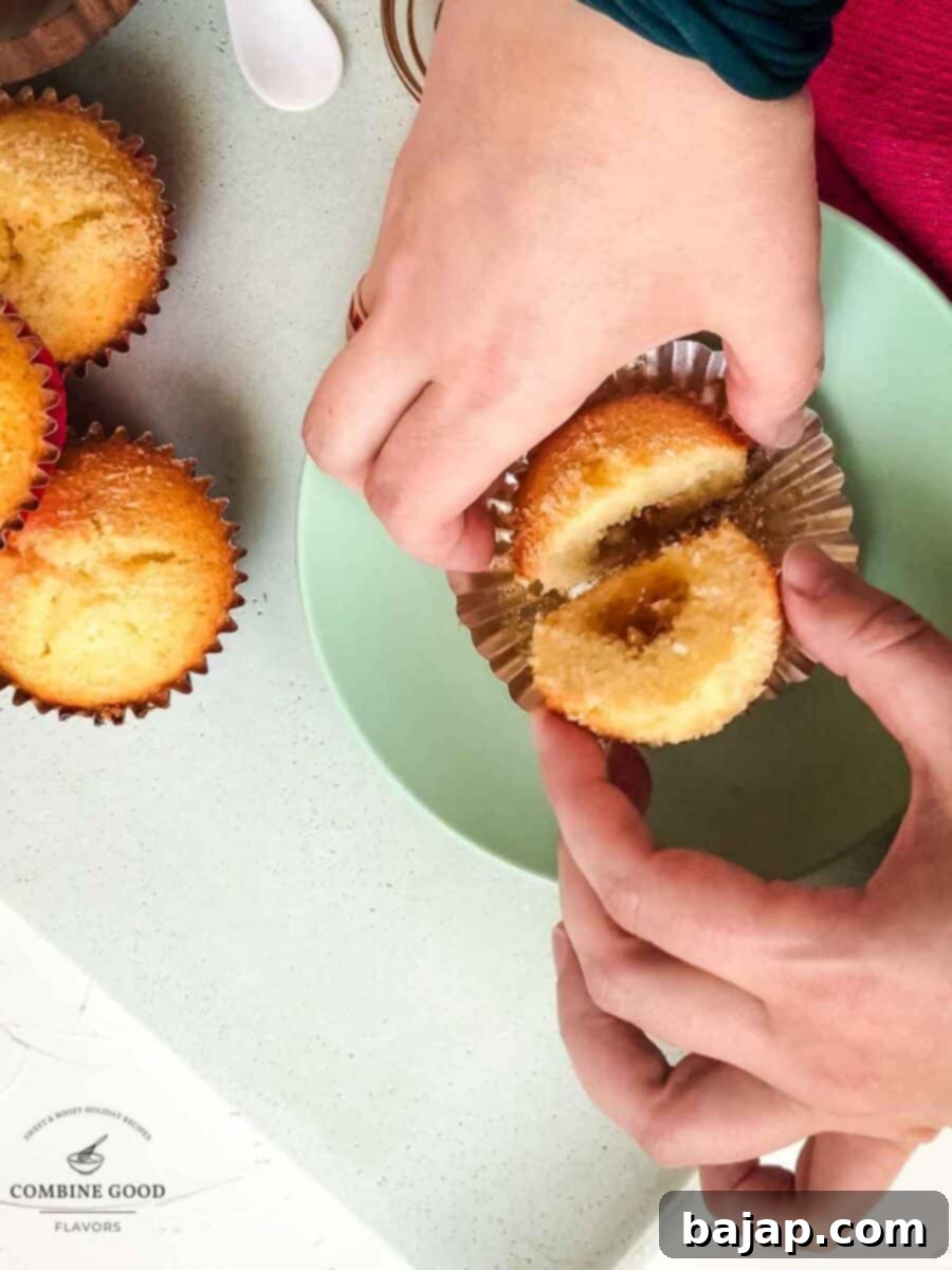 Hands gently separate a sliced coconut muffin, clearly showing the warm, vibrant fig jam center.