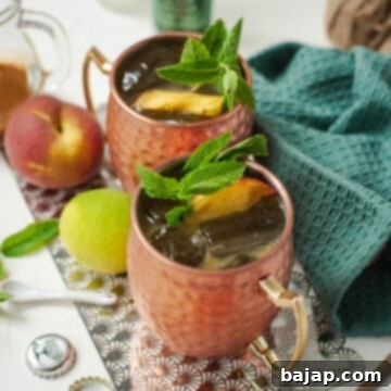 Delicious peach Moscow mule, served in copper mugs, garnished with peach slices and mint.