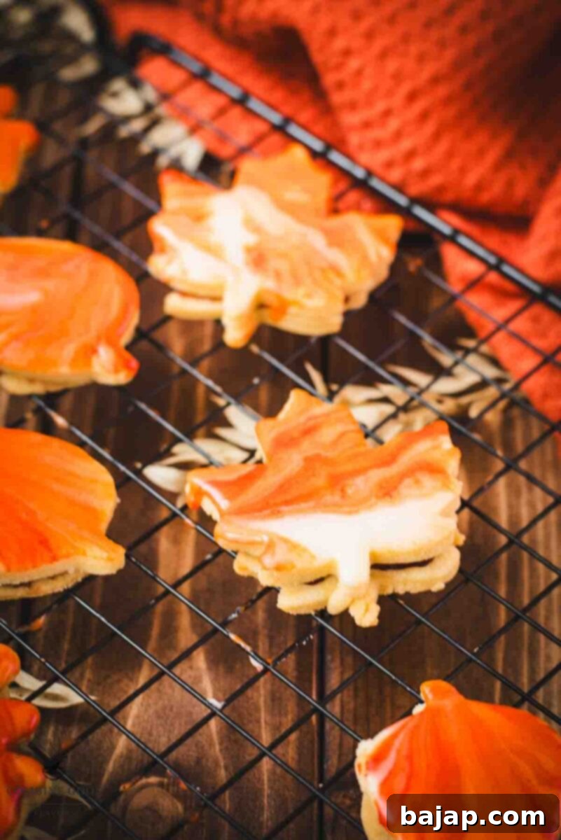Beautifully crafted leaf-shaped sandwich cookies with a vibrant marbled orange glaze, filled with sweet raspberry jam, perfect for fall.