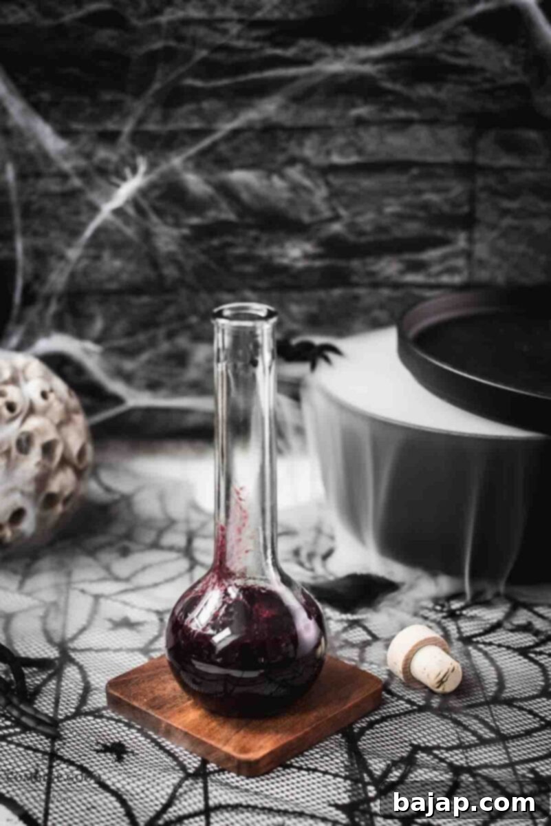 Easy 3-Ingredient Fake Blood 4 Eerily beautiful, decorated with cobwebs and a black, steaming cauldron, showcasing a bottle of the finished berry blood syrup.