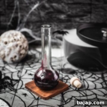 Easy 3-Ingredient Fake Blood 6 Glass bottle filled with berry blood Halloween syrup. Eerily beautiful, decorated with cobwebs and a black, steaming cauldron, setting a spooky mood.