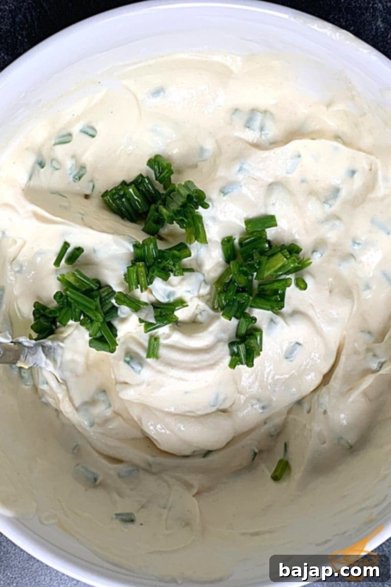Whip Up Delicious Homemade Chive Sauce in 5 Minutes 2 Creamy chive sauce in a white bowl, garnished with fresh chives, next to a spoon.