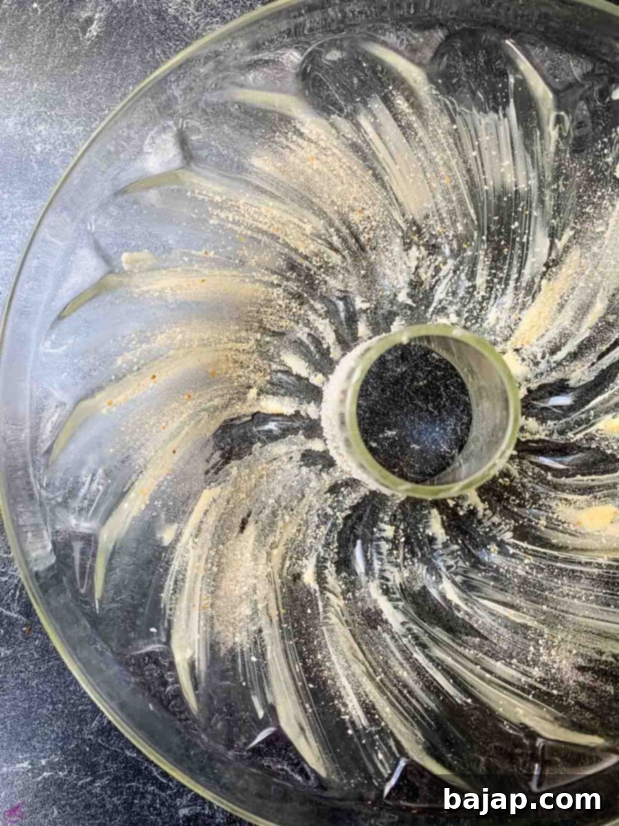 Preparing a bundt cake pan by thoroughly coating it with butter and dusting evenly with breadcrumbs to prevent sticking.