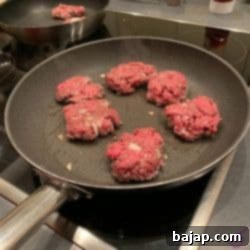Mini burger patties sizzling in a hot skillet.