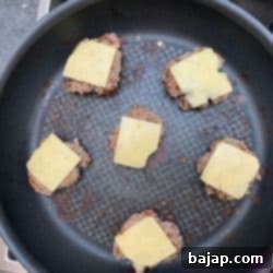 Cheddar cheese melting on mini burger patties in the pan.