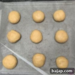 Mini burger buns rising on a baking sheet before baking.