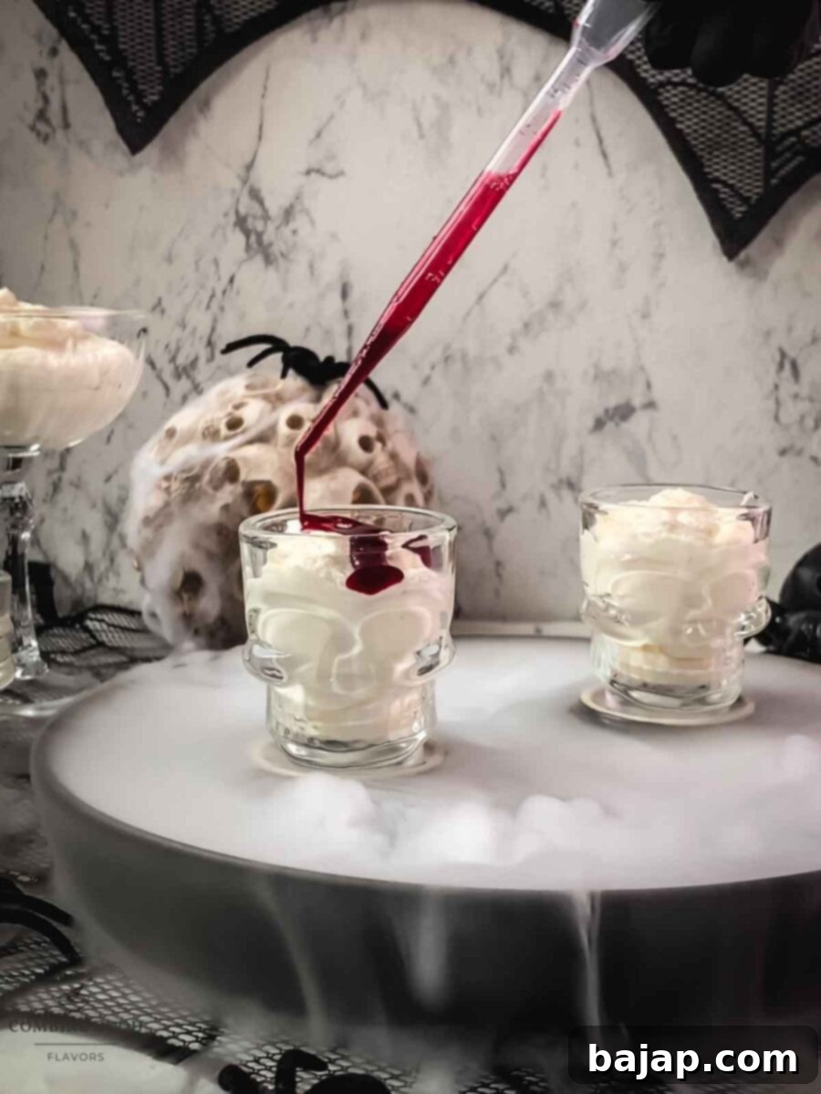 Drizzle with berry blood syrup. A hand is drizzling dark red berry blood syrup over a white mousse in a skull-shaped glass, creating a visually striking 'blood clot' effect. The mousse has visible red streaks from earlier swirling.